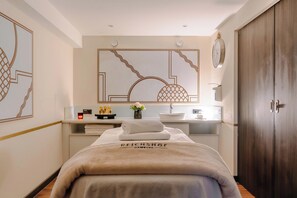 Une chambre d’hôtel avec un lit, un grand miroir, une armoire en bois, un lavabo et un petit vase avec des fleurs.