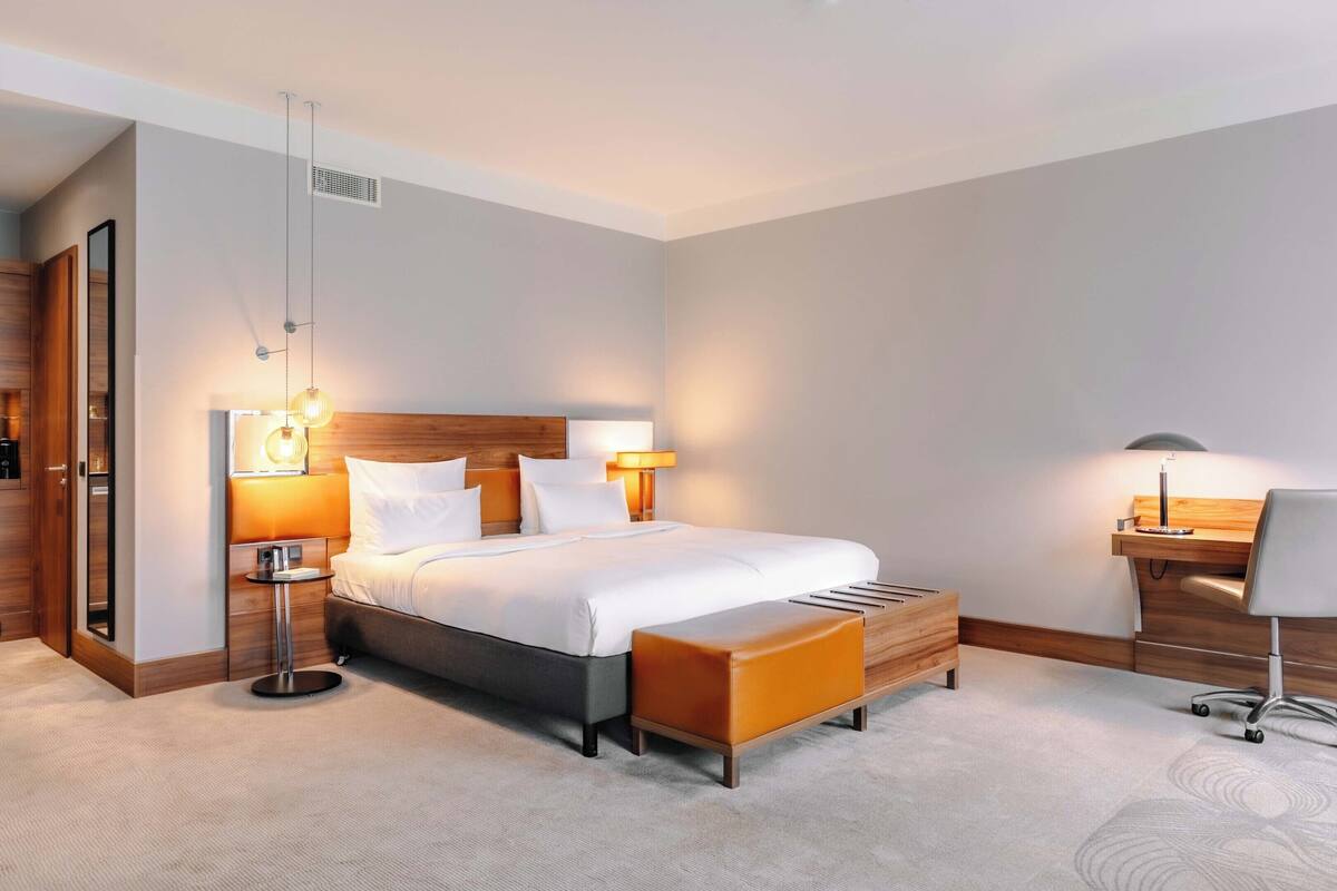 Une chambre d’hôtel moderne avec un grand lit, des lampes de chevet, un bureau en bois et un fauteuil confortable.