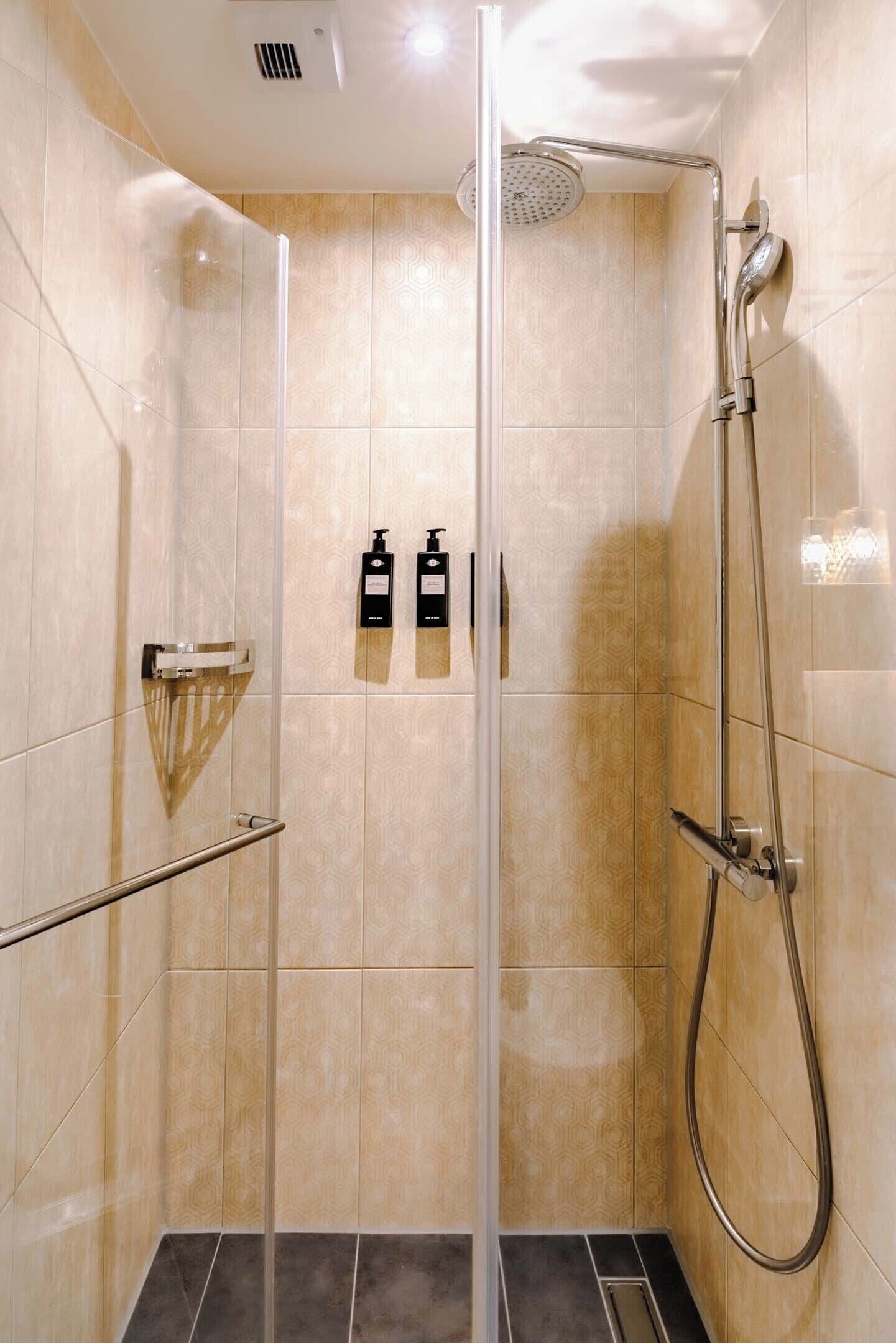 Una ducha moderna con puerta de vidrio, un cabezal de ducha manual y dos botellas de champú en la pared.