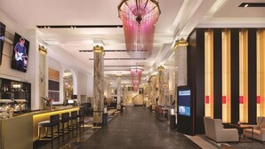Eine großzügige Hotelhalle mit Barbereich, Marmorsäulen und einem imposanten Kronleuchter.