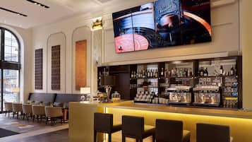 A bar area with a large TV screen, bar counter, seating, and a view of the street outside.