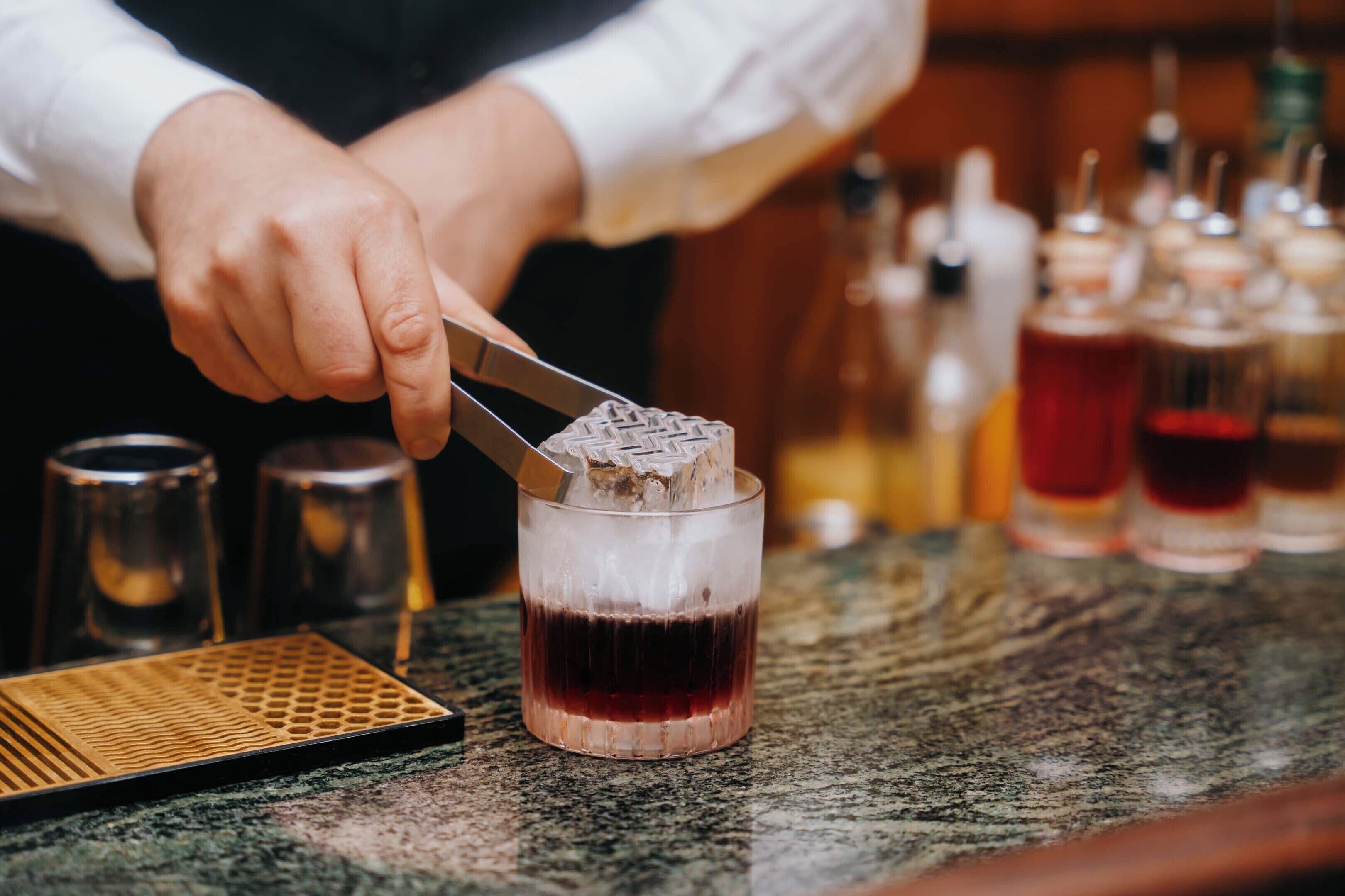 A bartender preparing a drink with a shaker and a glass on a bar counter.
