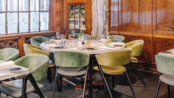 Un comedor con una mesa redonda dispuesta para seis personas, rodeada de sillas tapizadas en tono verde.