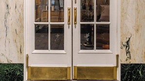 Ein Doppeltürer Eingang mit Glasscheiben und goldenen Griffen, oben beschriftet mit 