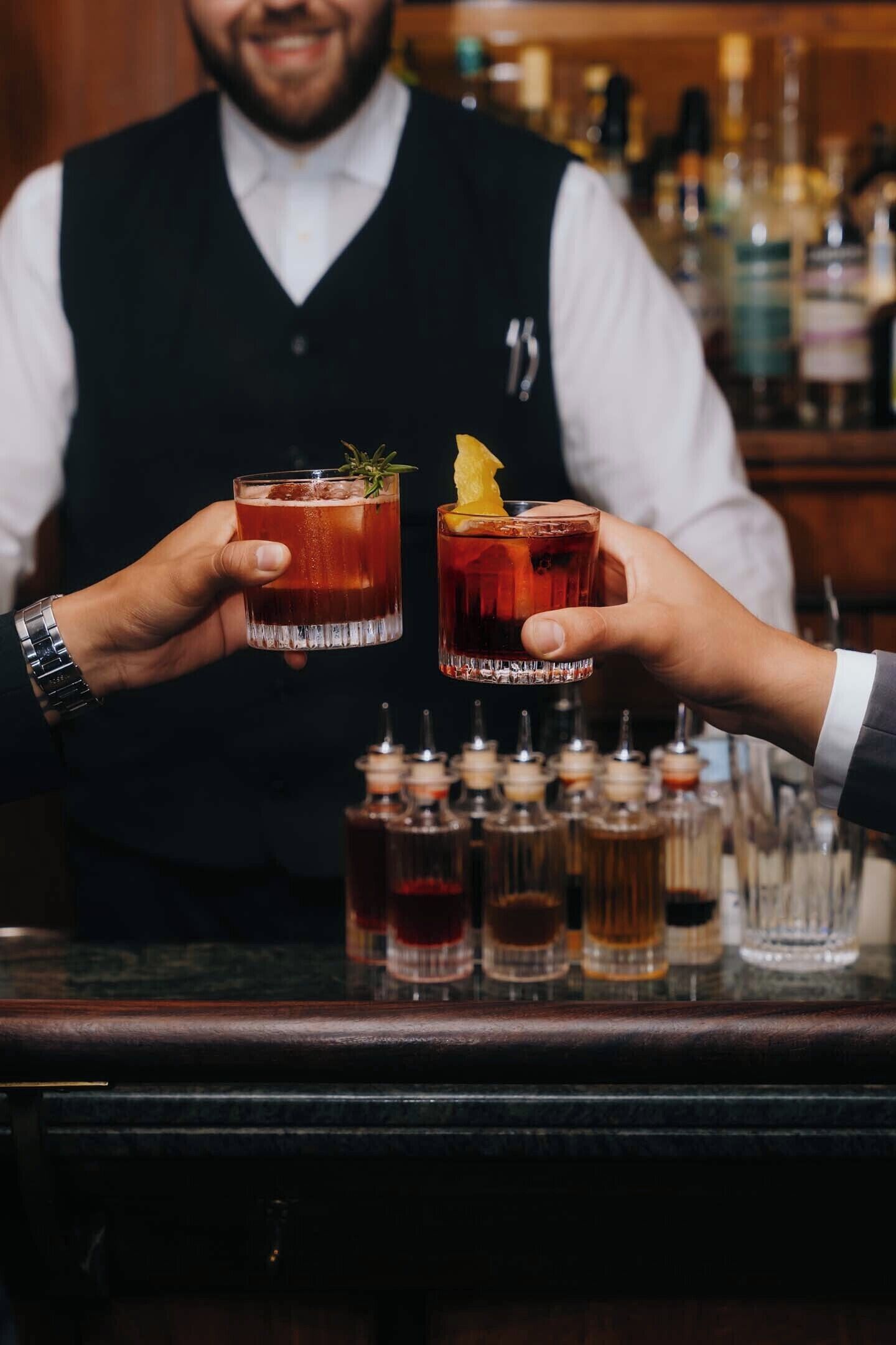 Ein Barkeeper hält zwei Gläser mit einem roten Getränk und einer Garnitur.