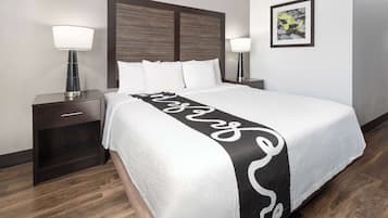 A neatly made bed with a white and black decorative runner, two bedside lamps, a dark wooden nightstand, and a framed picture on the wall.