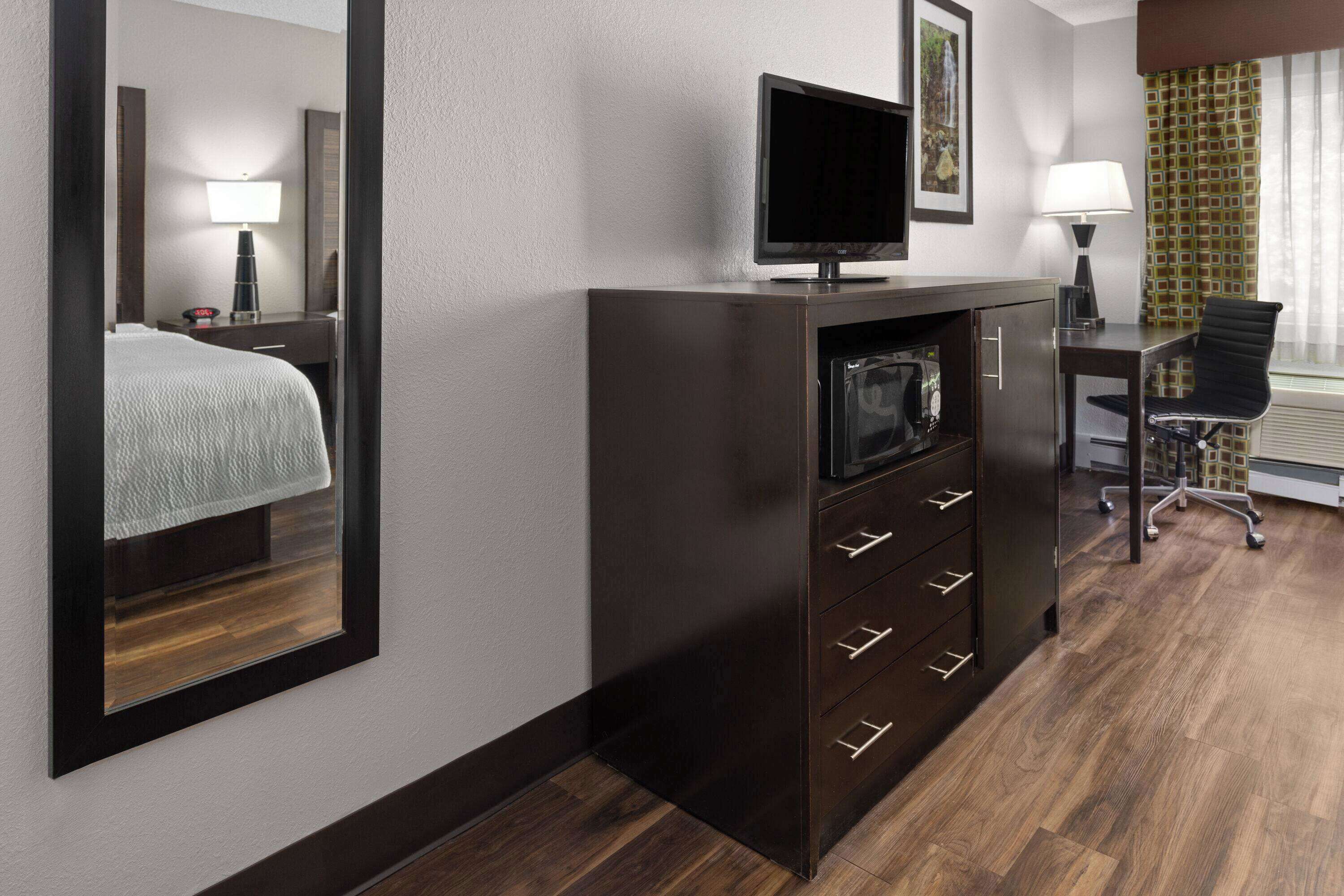 A hotel room with a bed, a TV, a desk with a chair, and a mirror.