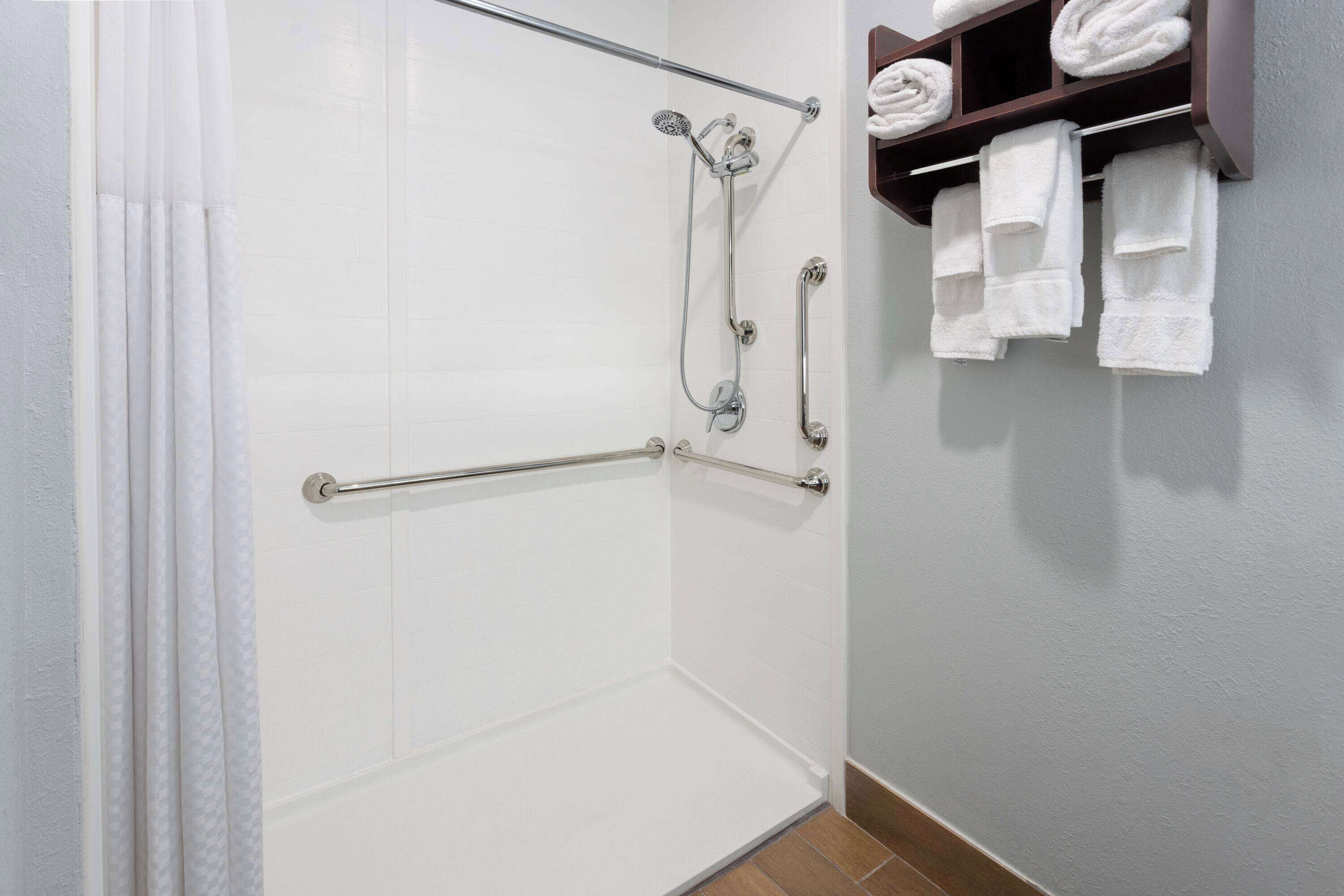 A shower area with a grab bar, a towel rack with towels, and a showerhead.