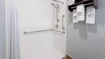 A shower area with a grab bar, a towel rack with towels, and a showerhead.