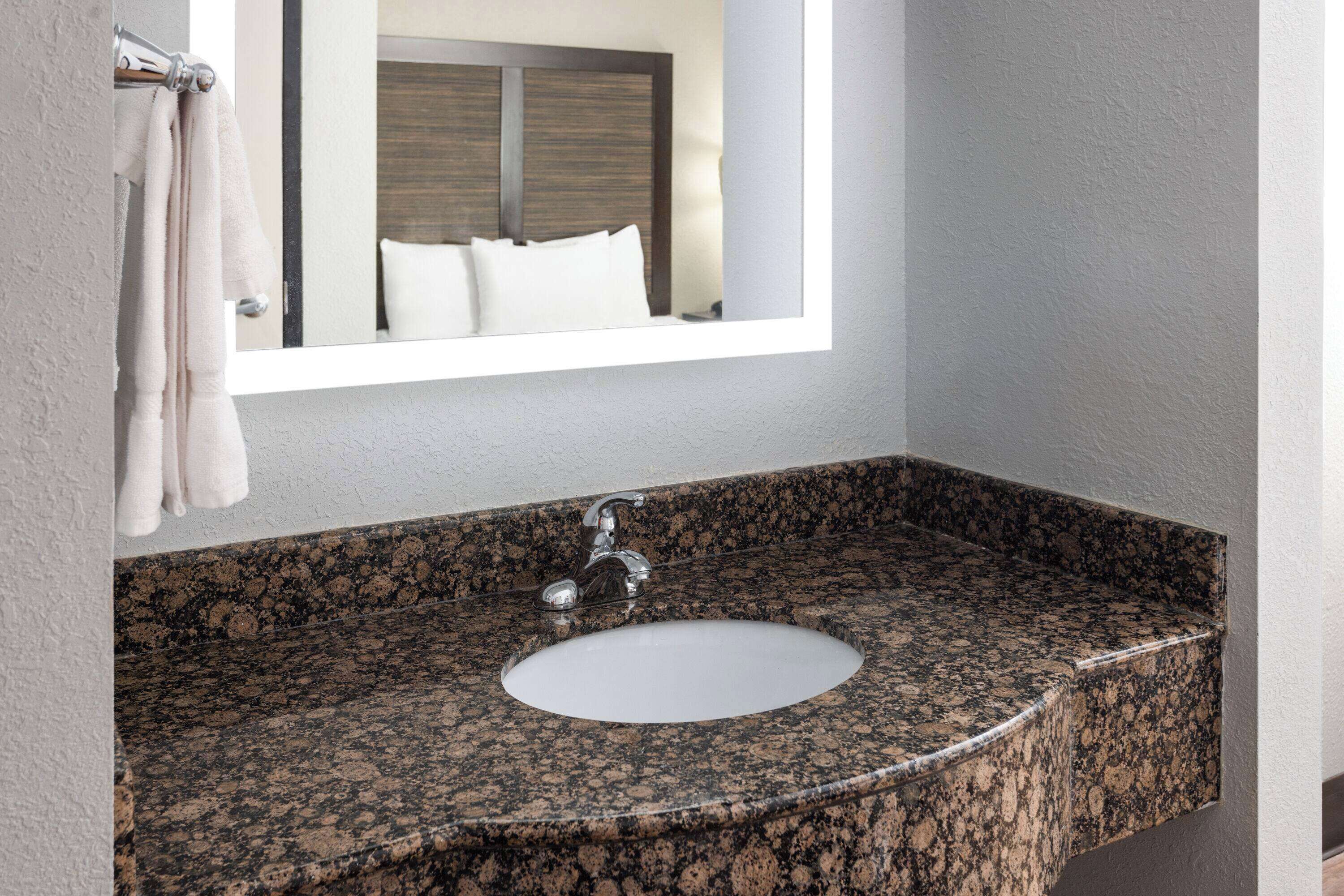 A bathroom with a granite countertop sink, a mirror, and a towel rack.