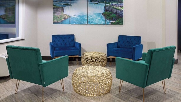 Une pièce avec deux fauteuils bleus, un fauteuil vert et un pouf en osier. Un grand tableau représentant un paysage est accroché au mur.