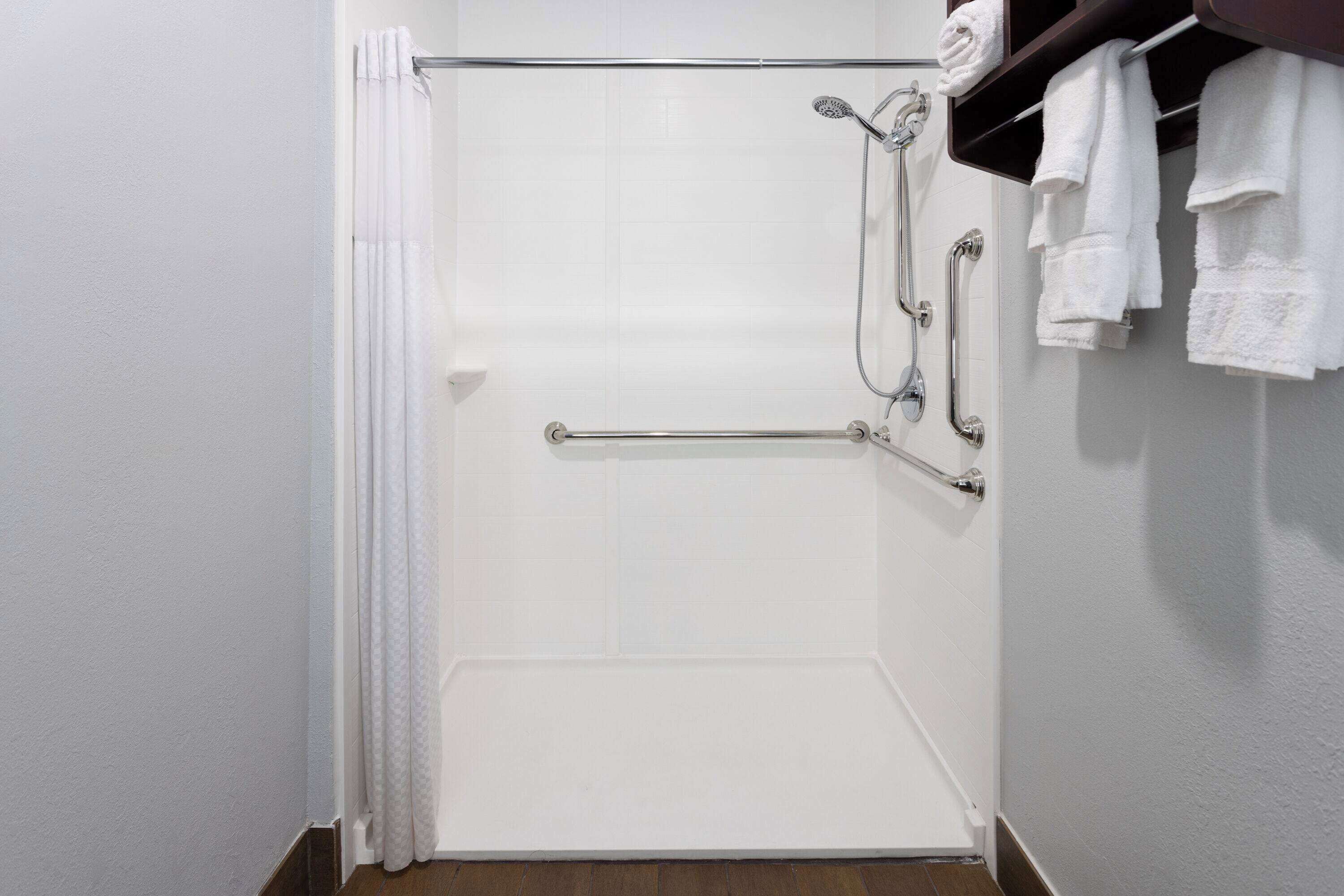 Eine weiße Dusche mit Glastür, einem Handtuchhalter mit Handtüchern und einer Haltestange.