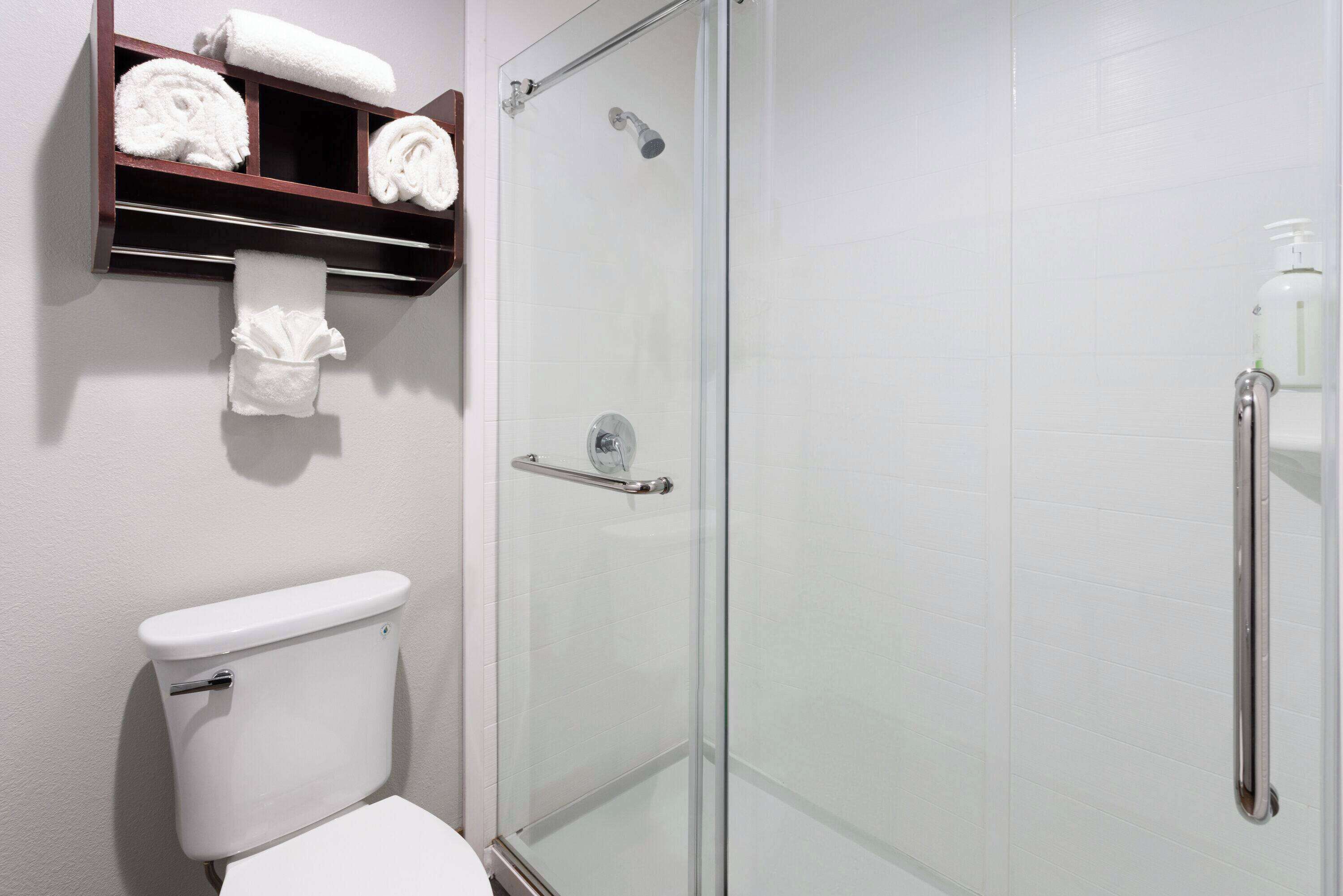 Un baño con inodoro, ducha con cerramiento de vidrio y repisa con toallas.