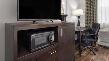 A hotel room with a flat-screen TV, a microwave, a desk with a lamp, and a chair.