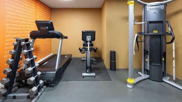 Un gimnasio con cinta de correr, mancuernas y máquina de pesas.