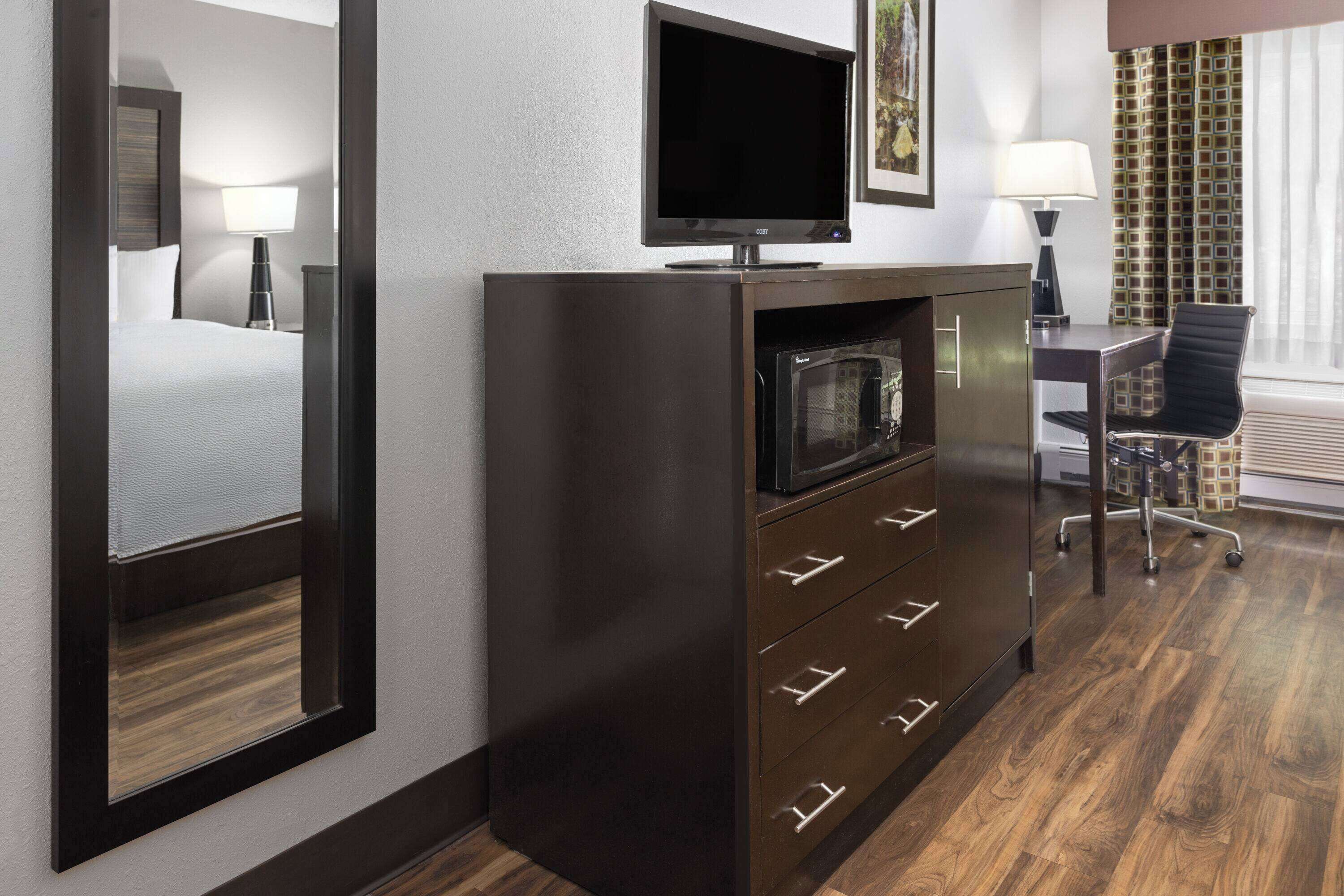 Habitación de hotel con cama, televisión sobre un mueble, escritorio con silla y ventana con cortinas.