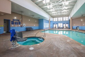 An indoor swimming pool with a lifeguard chair and a bench, surrounded by blue walls and large windows.