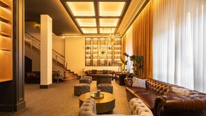 Un hall d’entrée spacieux avec un plafond haut, un grand escalier, des canapés en cuir et un lustre bien éclairé.