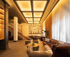 A spacious lobby with a high ceiling, a grand staircase, leather sofas, and a well-lit chandelier.