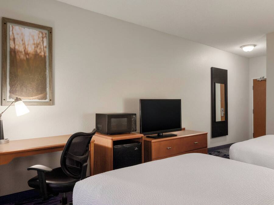 A hotel room with a desk, a television, a microwave, a chair, and two beds.