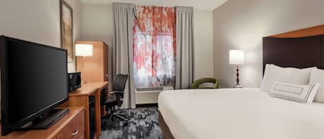 Habitación de hotel con una cama grande, un televisor de pantalla plana, un escritorio con una silla, una lámpara y un ventanal con cortinas.
