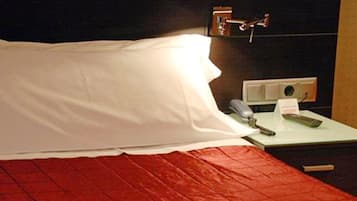 Habitación de hotel con cama, mesita de noche con teléfono y libreta, y toma de corriente.