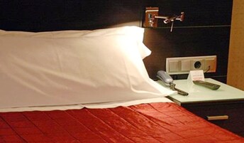 A hotel room with a bed, a bedside table with a telephone and a notepad, and a wall socket.