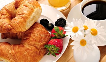 Ein Frühstückstisch mit Croissants, Erdbeeren, Brombeeren und einer Tasse Kaffee.