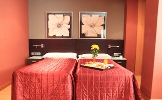 Ein Hotelzimmer mit zwei Betten, einem Nachttisch, einer kleinen Kommode und einem Tablett mit Frühstücksgebäck.