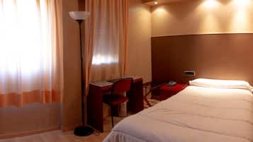 A hotel room with a bed, desk, chair, and lamp.