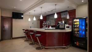 Zona de bar con mostrador, taburetes, televisor, luces colgantes, microondas y máquina expendedora.