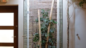 Una habitación con un separador de vidrio, una planta grande en maceta y una puerta con panel de vidrio esmerilado.