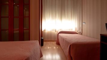 Habitación de hotel con dos camas, un ventanal con cortinas, un armario de madera y un altavoz.