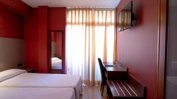A hotel room with two beds, a desk, a chair, a television, and a large window with curtains.