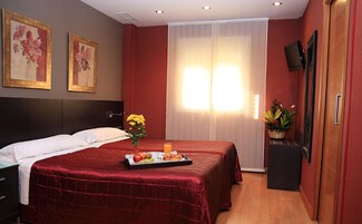 A hotel room with a large bed, a bedside table with a tray of fruit, a vase with flowers, and a television on the wall.