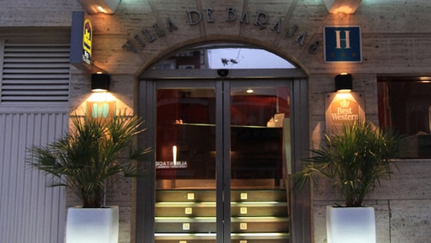 La entrada a Villa De Bacas, con un cartel sobre la puerta, dos macetas a cada lado y un cartel de 'Best Western' a la derecha.
