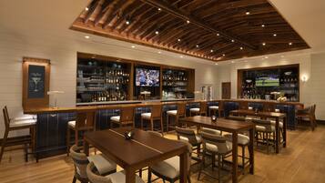 A bar area with wooden furniture, a television, and a variety of bottles and glasses.