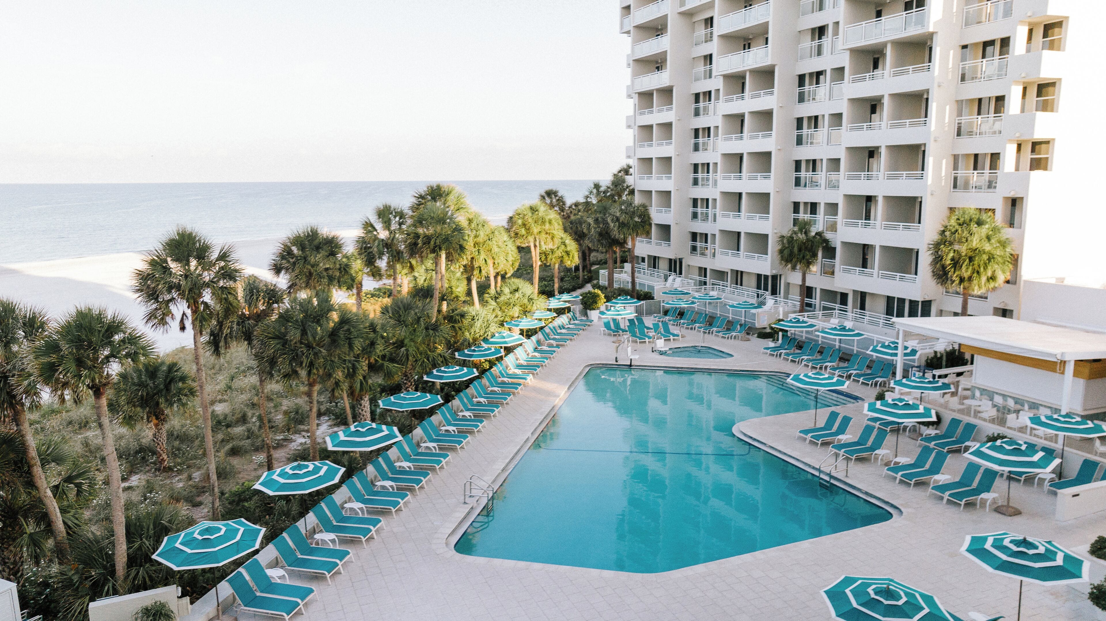 A resort pool area with multiple lounge chairs and umbrellas, a large swimming pool, and a view of the ocean.