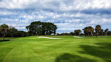 A well-maintained golf course with sand bunkers, lush green grass, and a variety of trees.