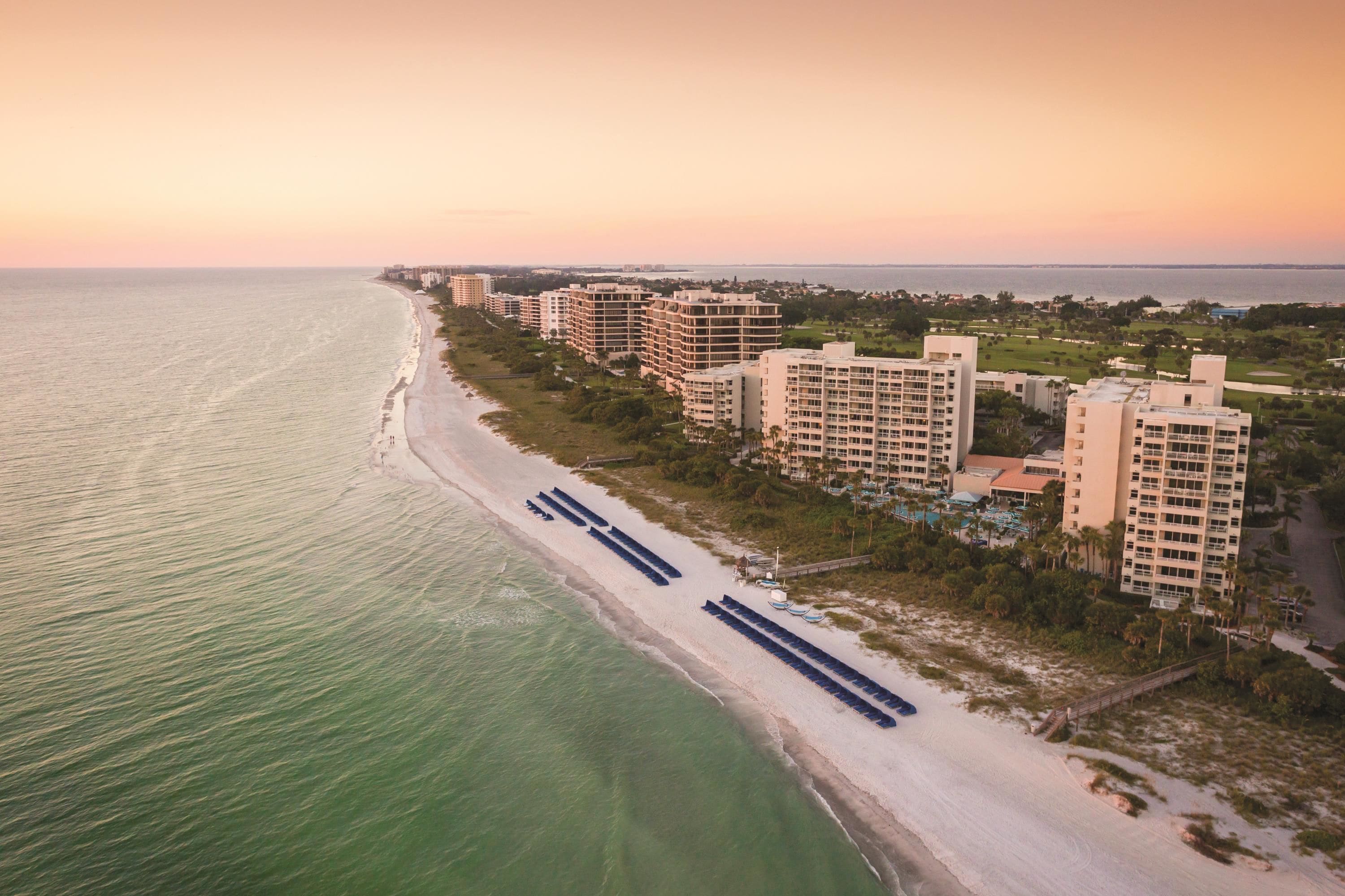 A coastal hotel with multiple high-rise buildings, a beach promenade, and a view of the ocean.