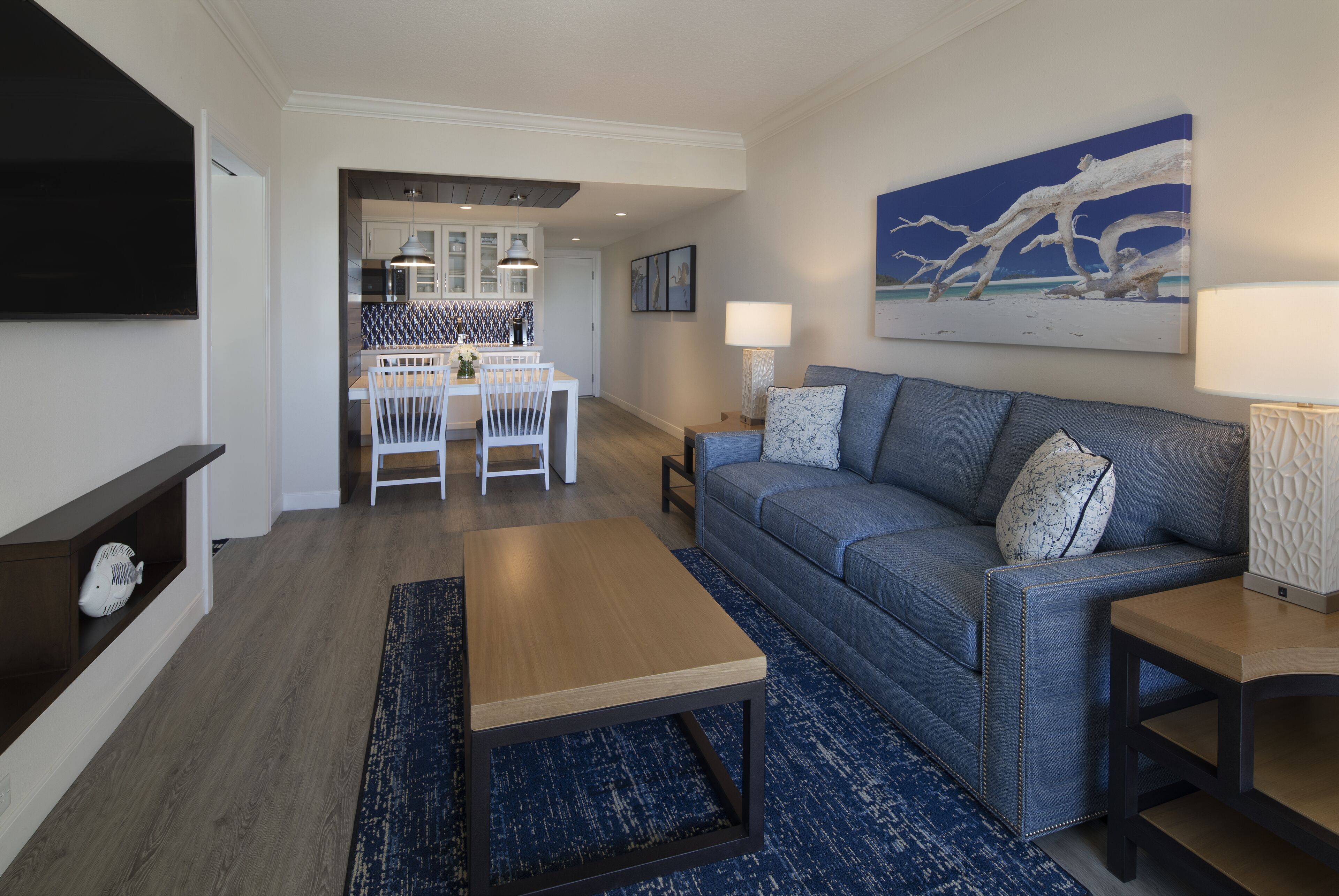 A modern living room with a blue sofa, a wooden coffee table, and a TV mounted on the wall.