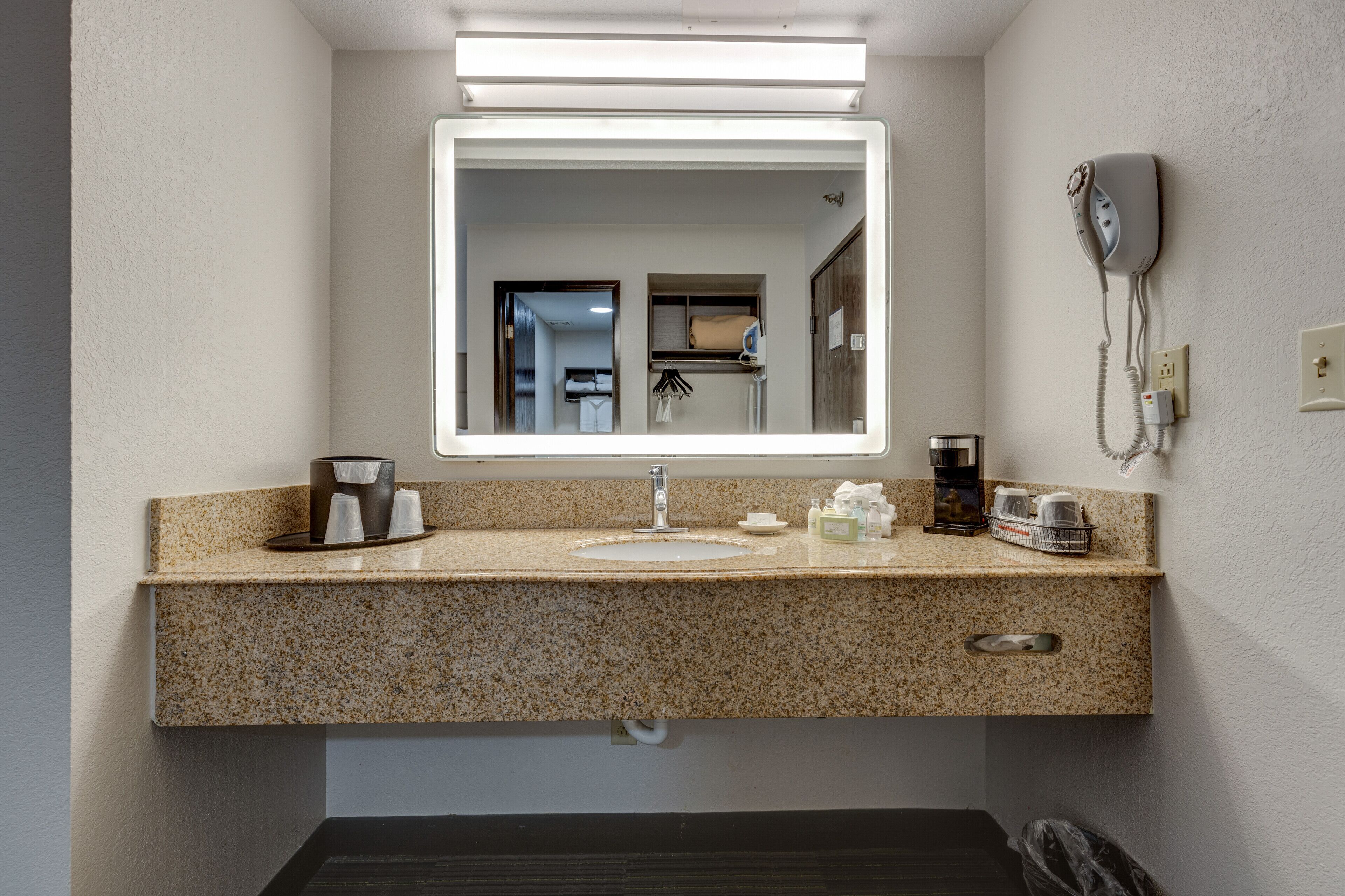 Bagno con piano di lavoro in granito, lavabo, specchio, asciugacapelli e porta asciugamani.