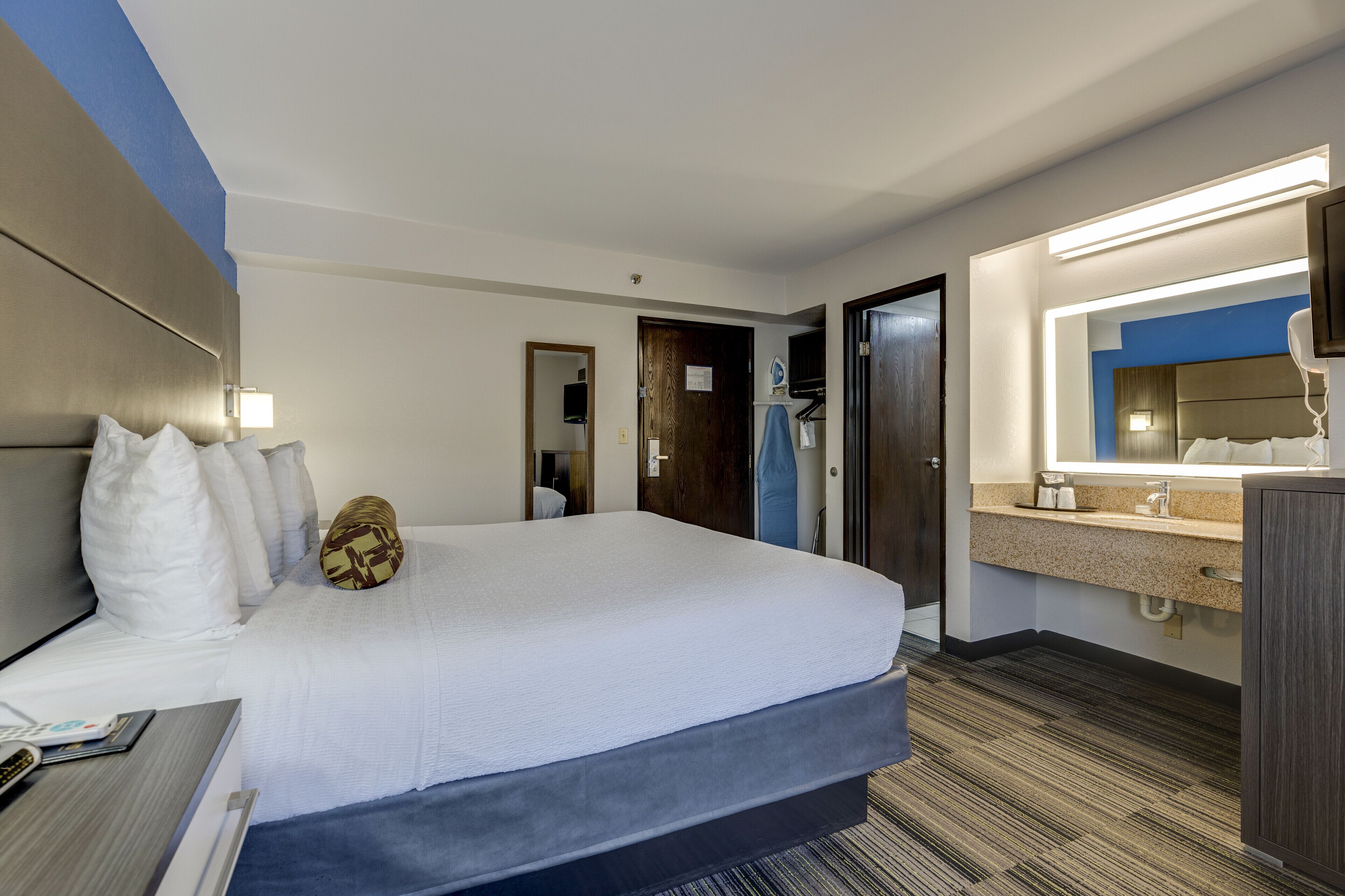 Ein Hotelzimmer mit einem großen Bett, einem Nachttisch mit Lampe, einem Badezimmer mit Spiegel und einem Fernseher.