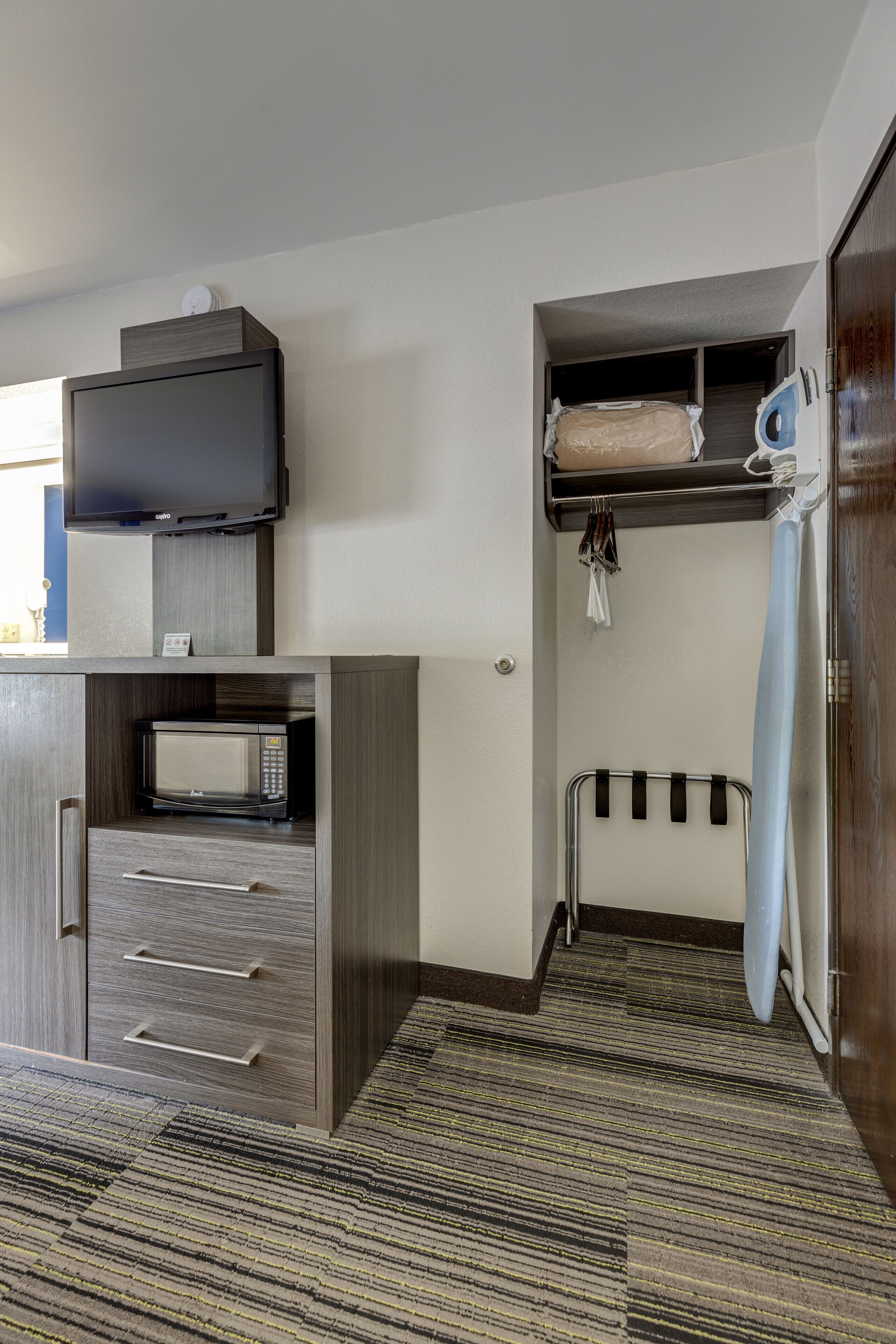 A compact hotel room with a kitchenette, including a microwave, a small refrigerator, and a television. There is a shower area with a towel rack and a hanging shower curtain.