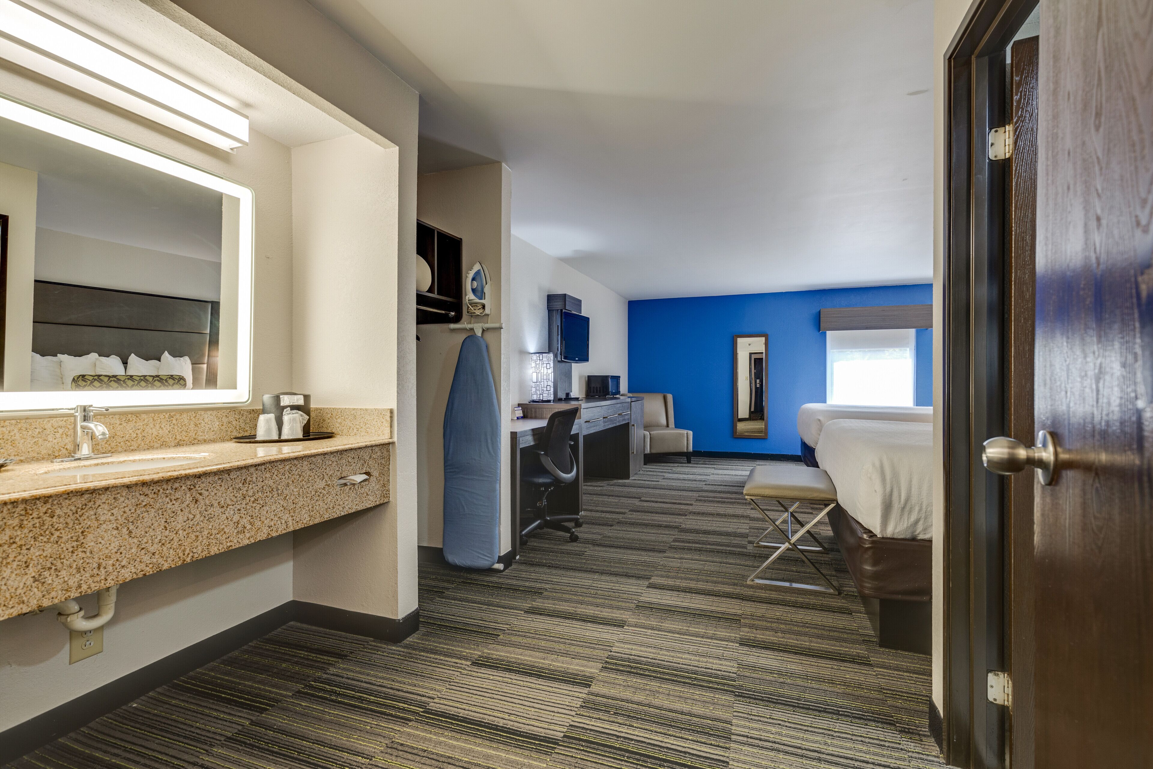 A hotel room with a bathroom, a desk, a bed, and a window.
