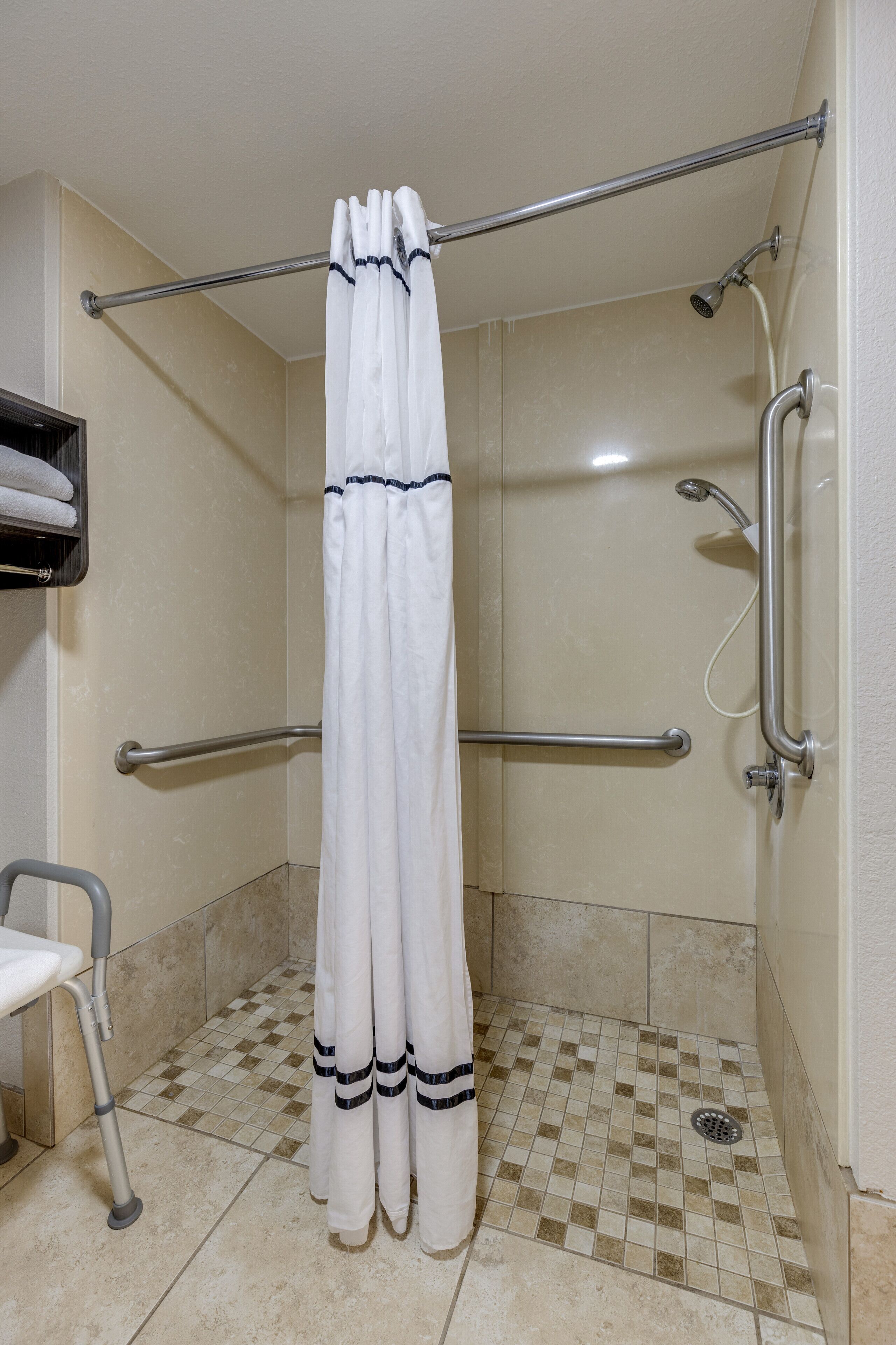 A shower area with a white curtain, grab bars, a handheld showerhead, and a tiled floor.