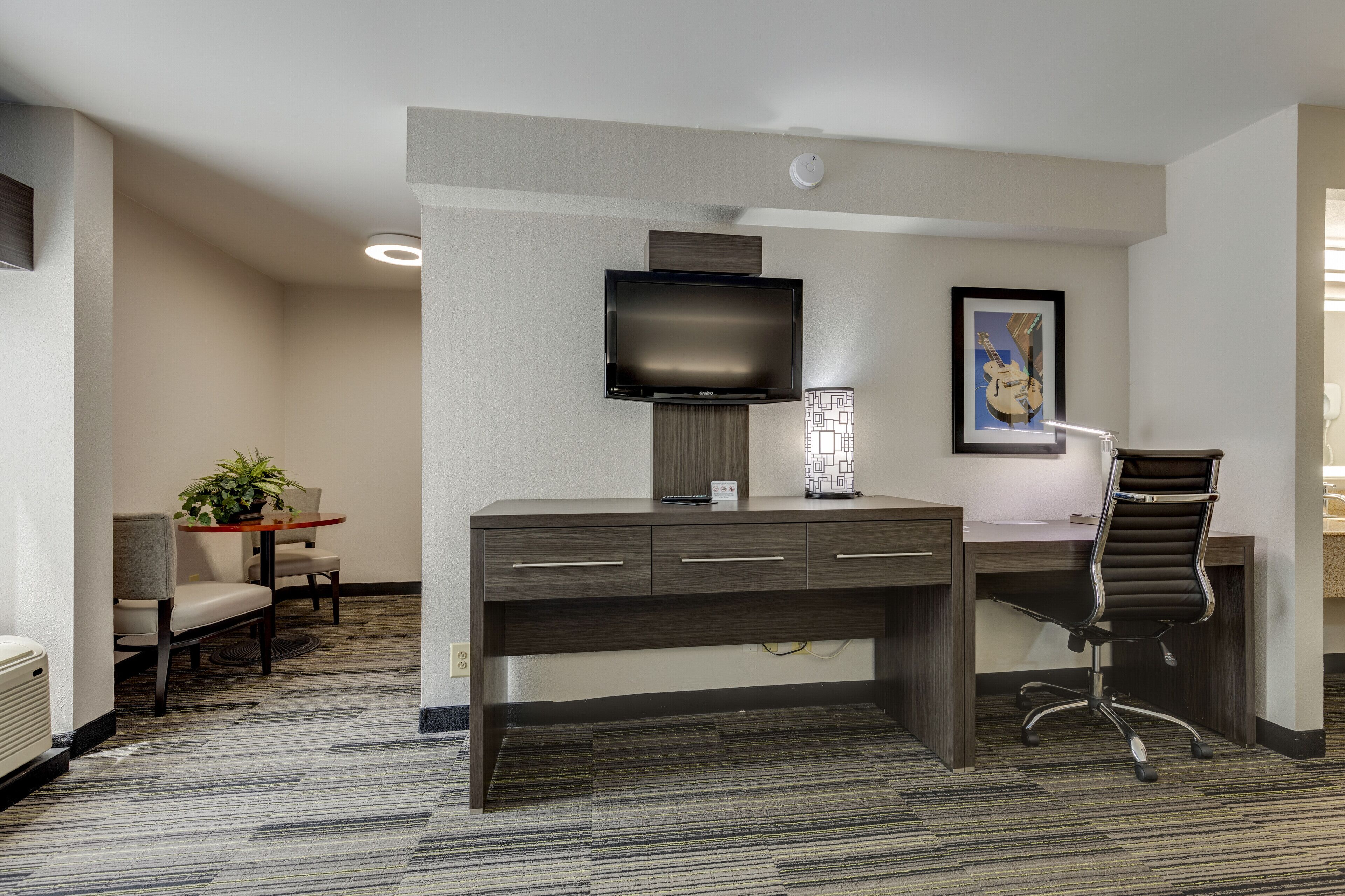 A hotel room with a desk, a chair, a television, and a framed picture on the wall.