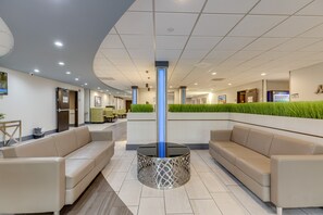 A modern lobby with a central glass column, beige sofas, and a green plant wall. - The Alexis Inn & Suites - Nashville Airport (Nashville)