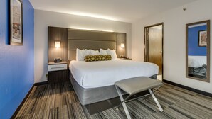 Habitación de hotel con una cama grande, mesitas de noche, un banco y un cuadro en la pared.