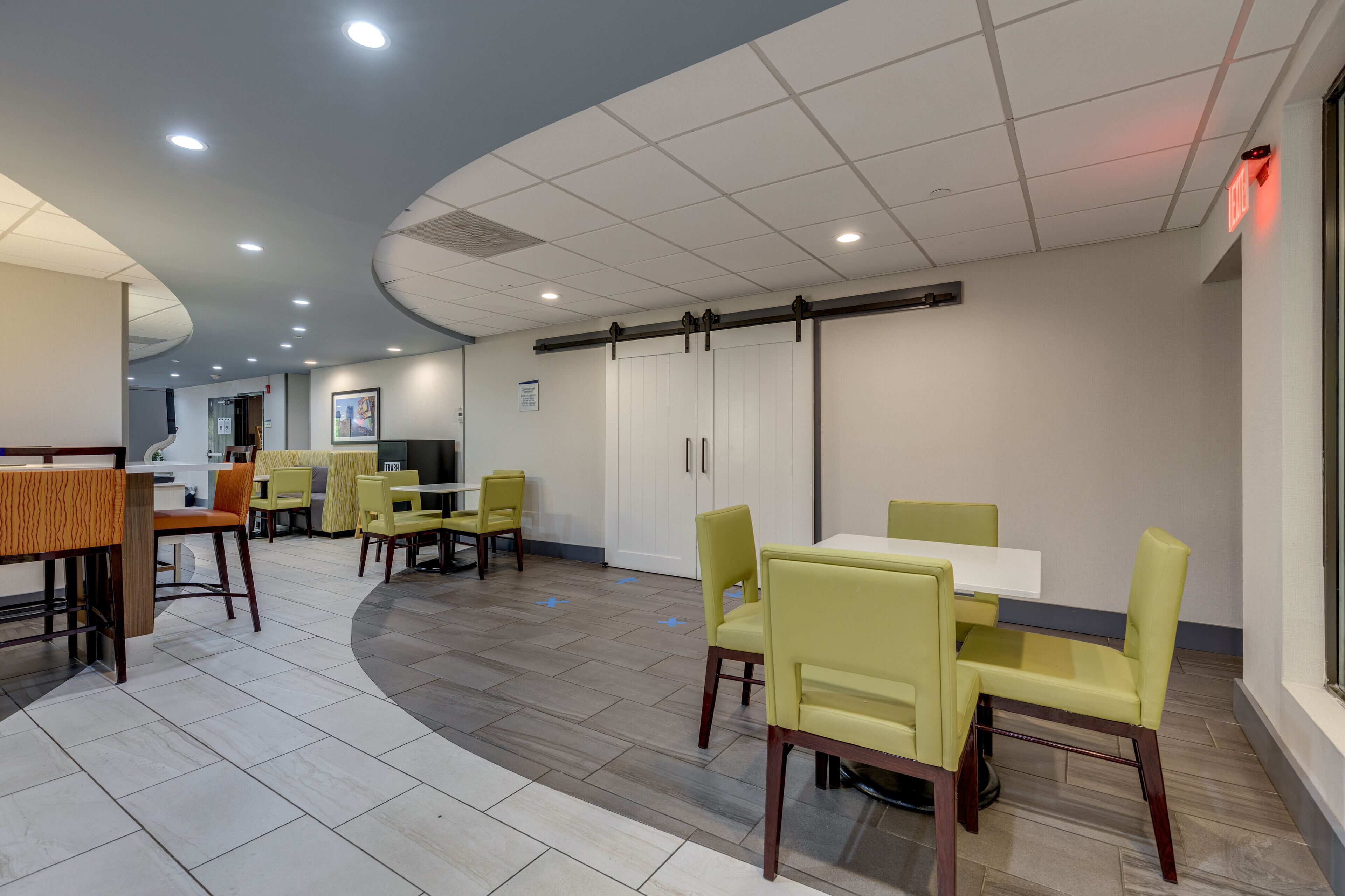 Een moderne eetruimte met gele stoelen en witte tafels, een gebogen plafond met ingebouwde verlichting, en een uitzicht op de keuken op de achtergrond.
